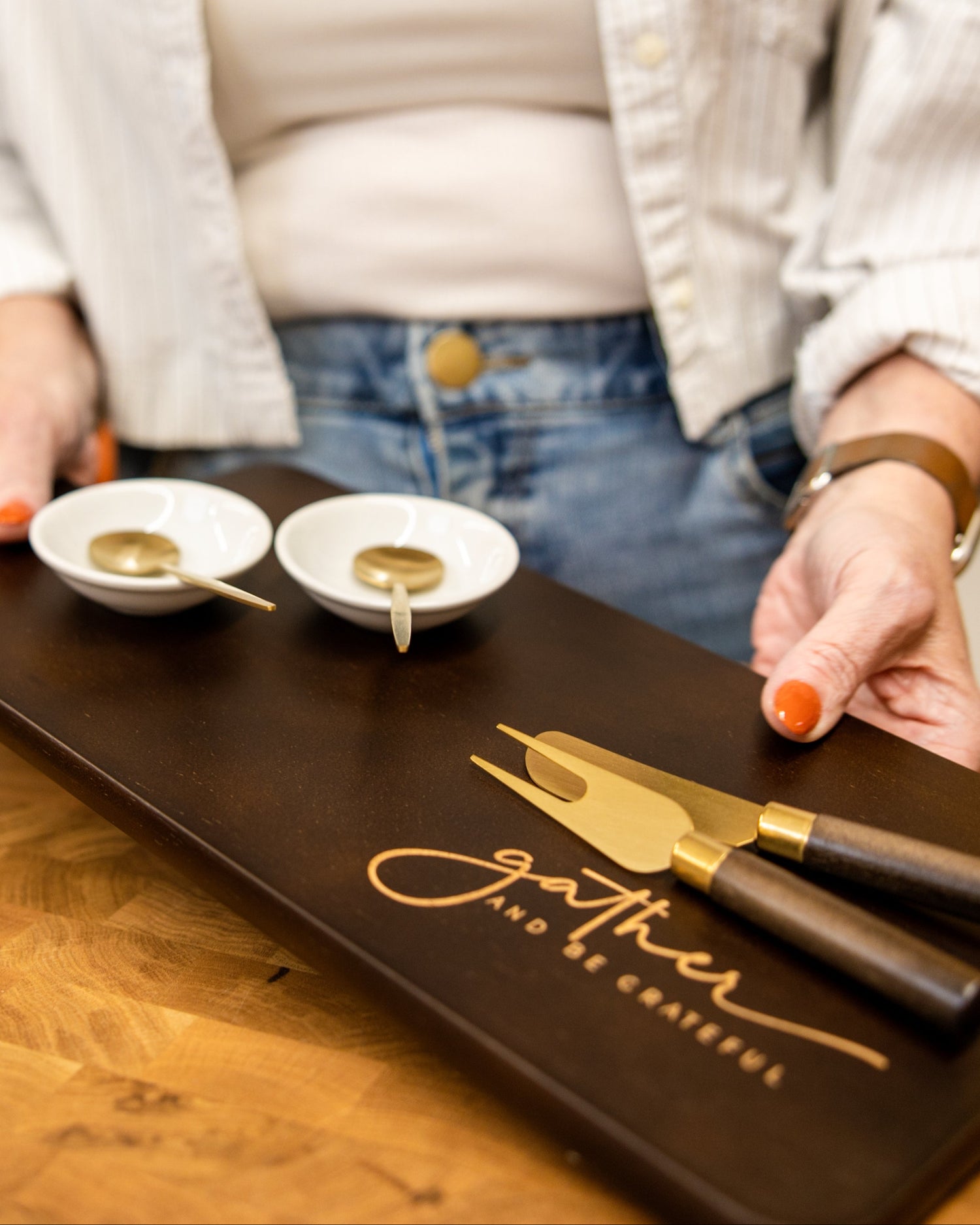 Owner holding a wooden tray with two small bowls and a knife on a wooden table.