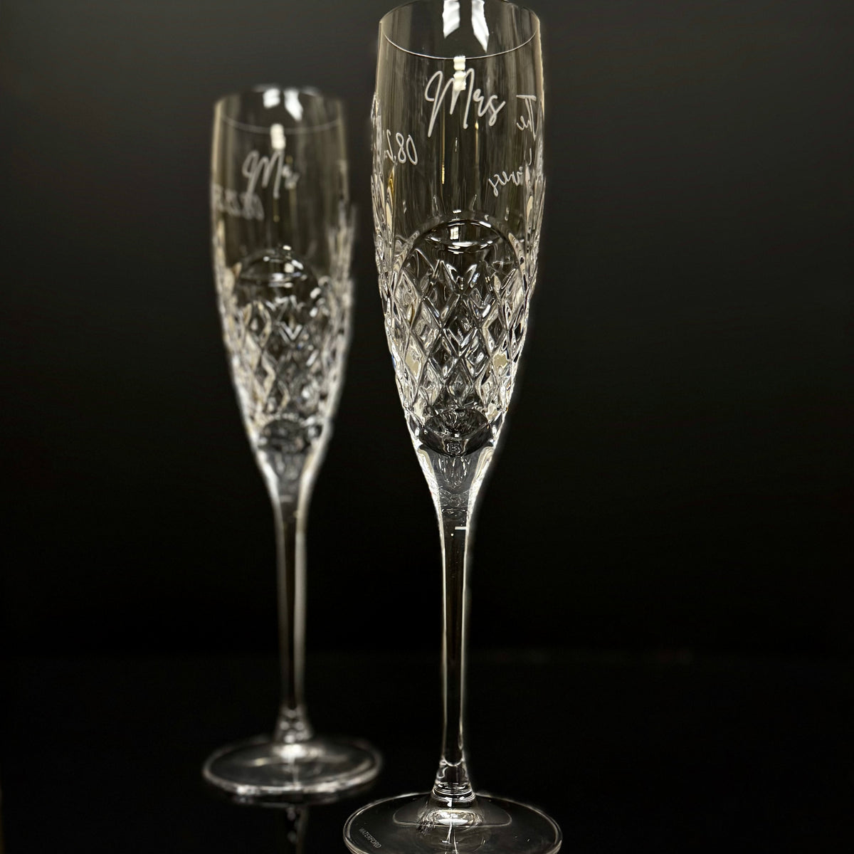 Two crystal champagne flutes with engraved text on a black background