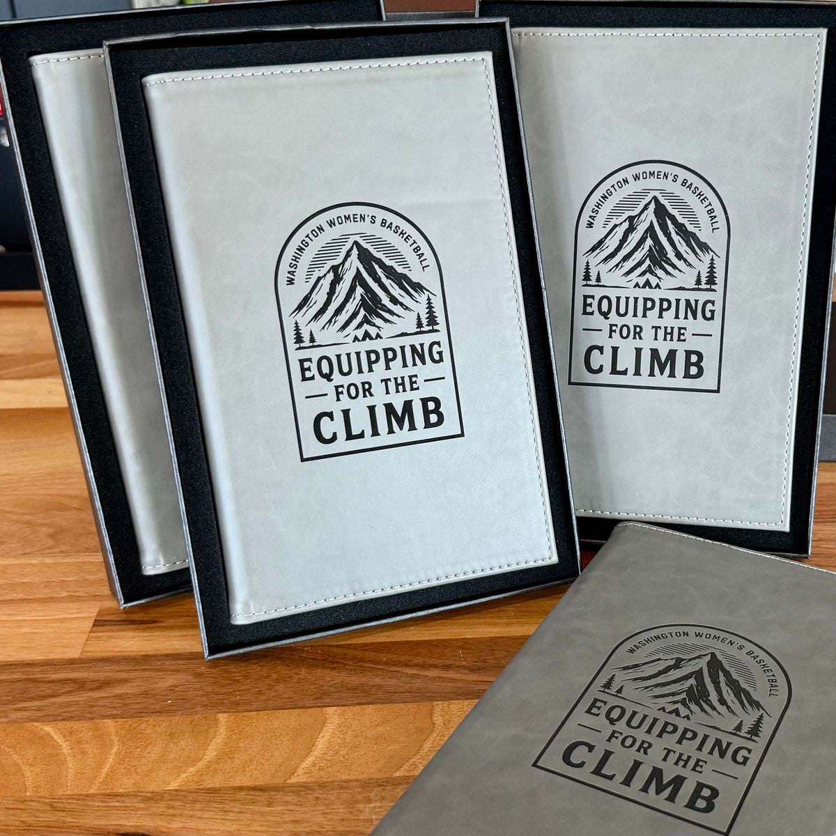 Gray corporate portfolios engraved with Washington Women’s Basketball Equipping for the Climb artwork and displayed in presentation boxes.