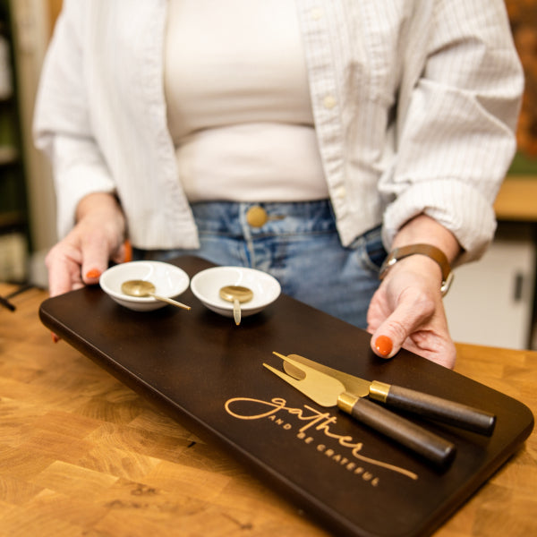 Person holding a wooden tray with two small bowls and a knife on a wooden table.