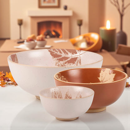 Three nesting stoneware bowls with fall leaf design and bare ceramic base.