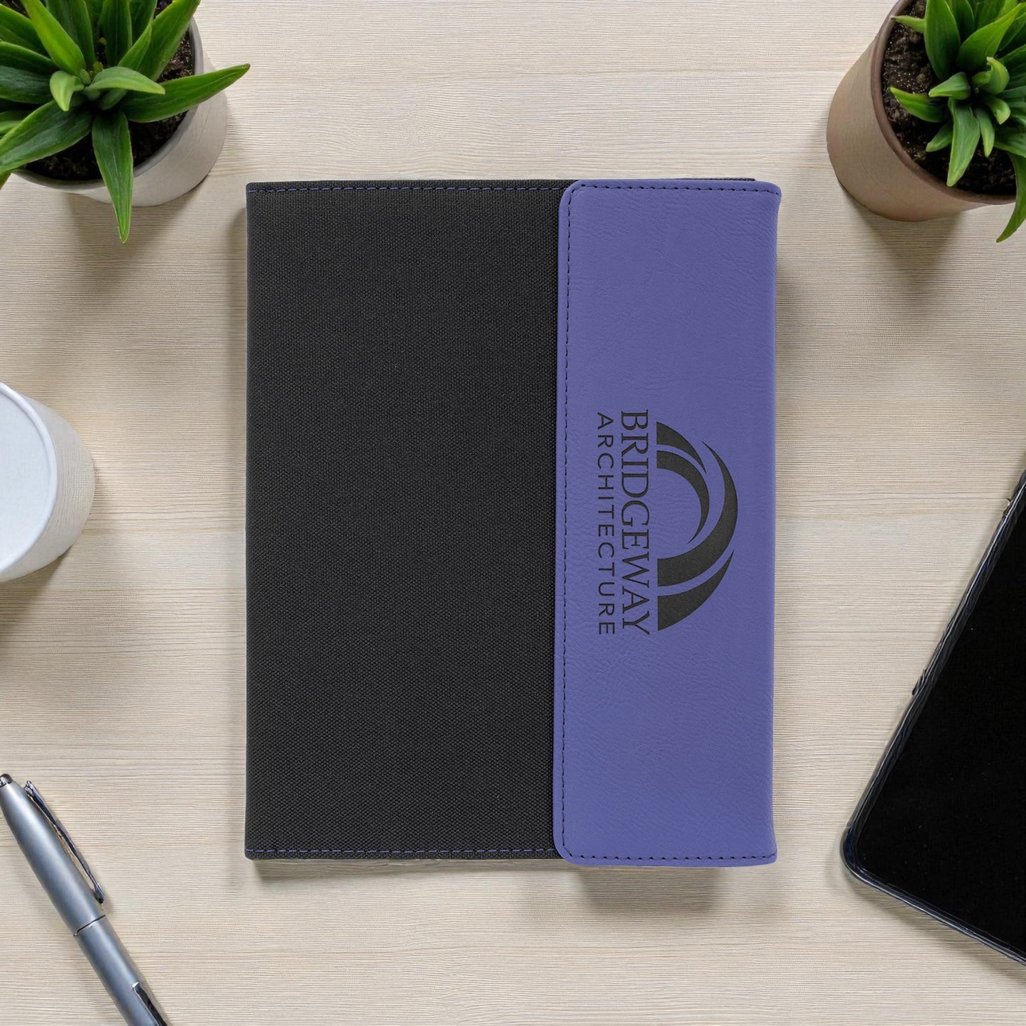 Black and purple notebook with Bridgeway Architecture logo on a desk with office supplies.