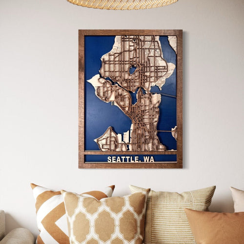 Wooden map of Seattle, WA in a frame on a wall with decorative pillows below.