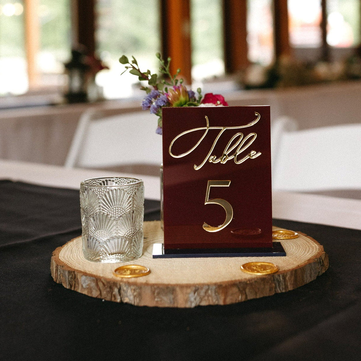 Burgundy and gold layered wedding table number displayed on a natural wood centerpiece.