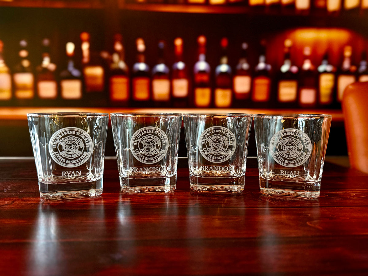 Four square whiskey glasses personalized with matching crest artwork and individual names.