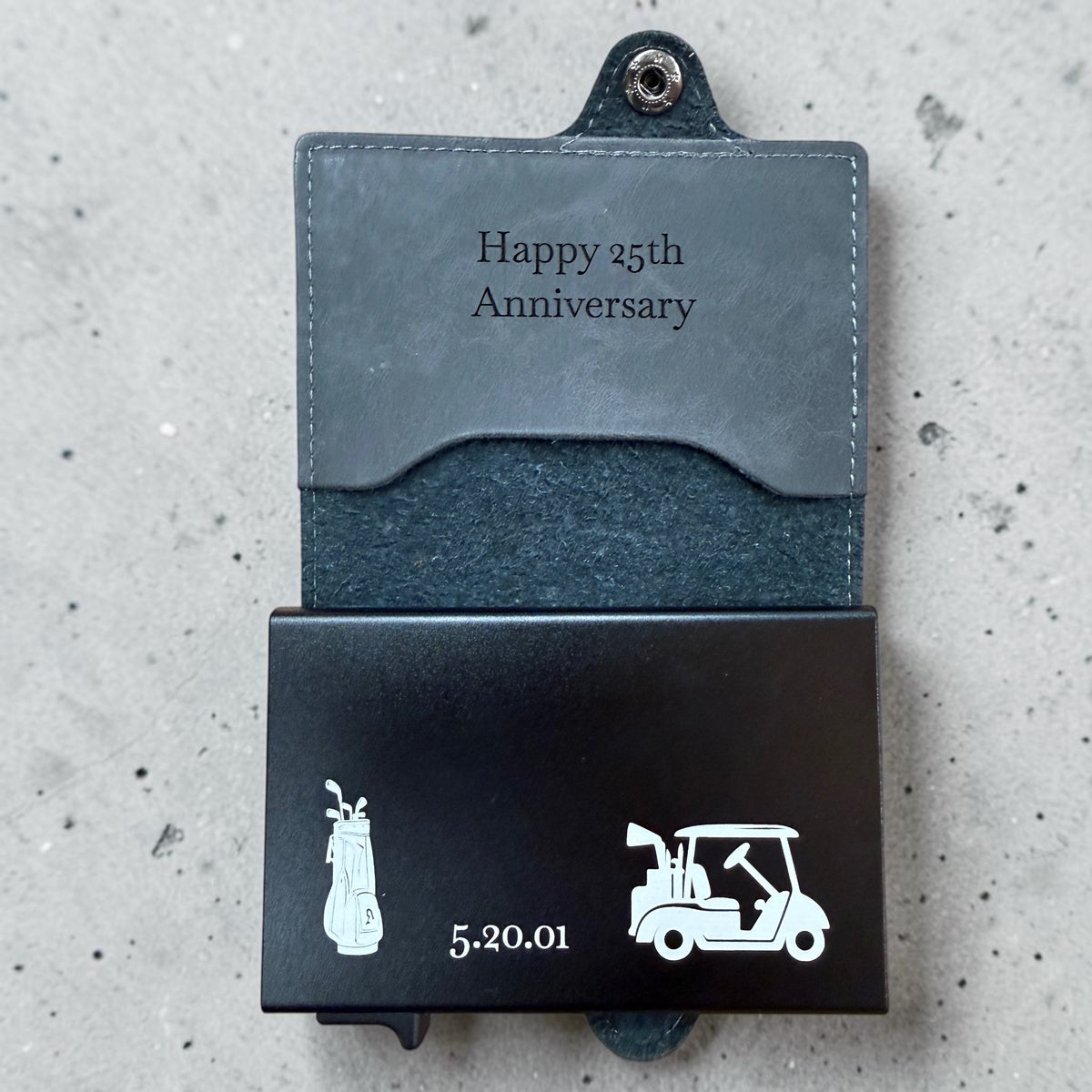 Black metal wallet and leather holder personalized with golf artwork, a 25th-anniversary message and the date May 20, 2001.