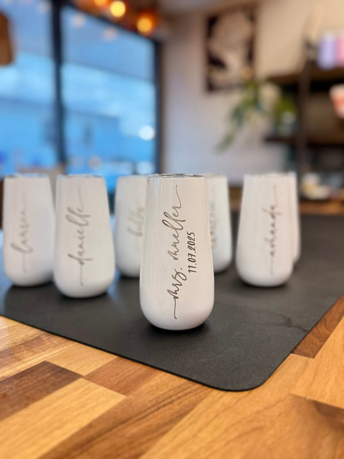 Group of white insulated champagne tumblers individually engraved with names and a wedding date.