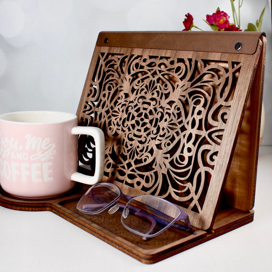 Wooden book stand with engraved front panel and coffee mug beside reading tray